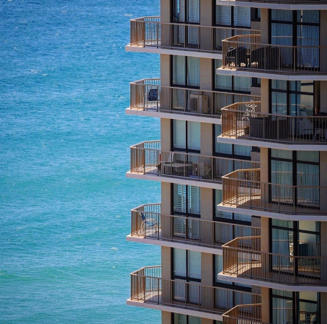 Stacked balconies of a beachfront tower cut hard against flat blue water.