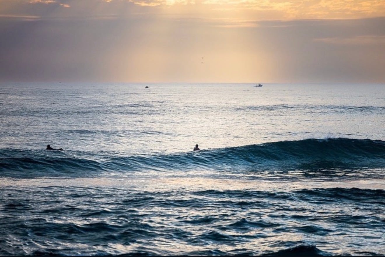 Two surfers sitting out the back at dawn, a clean unbroken line swinging towards them.